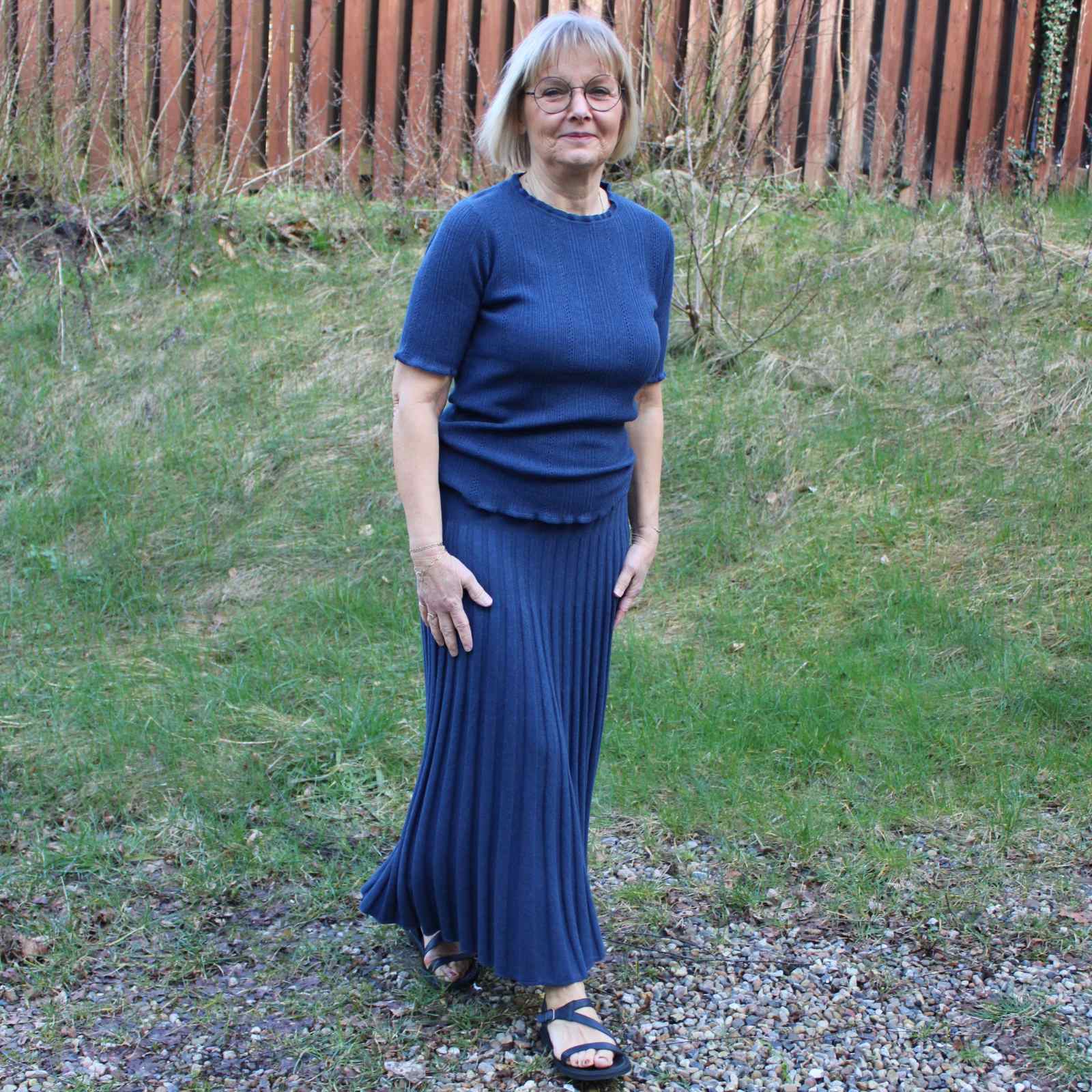 Anbi Jette i blå kortærmet bluse og blå nederdel med græs baggrund