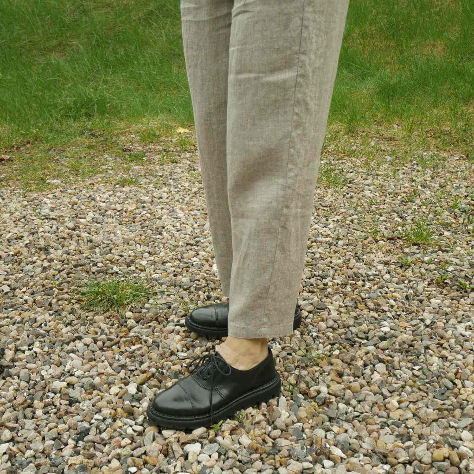 Bukseben på beige hørbukser med sorte sko på grus