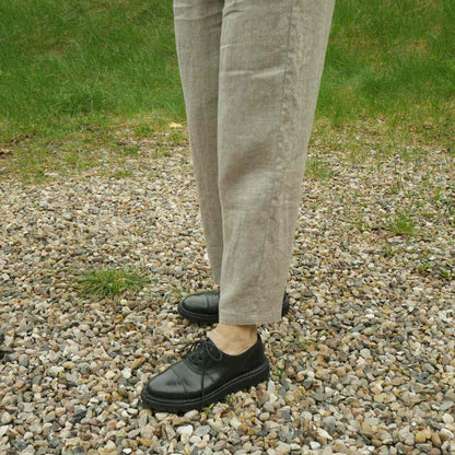 Bukseben på beige hørbukser med sorte sko på grus