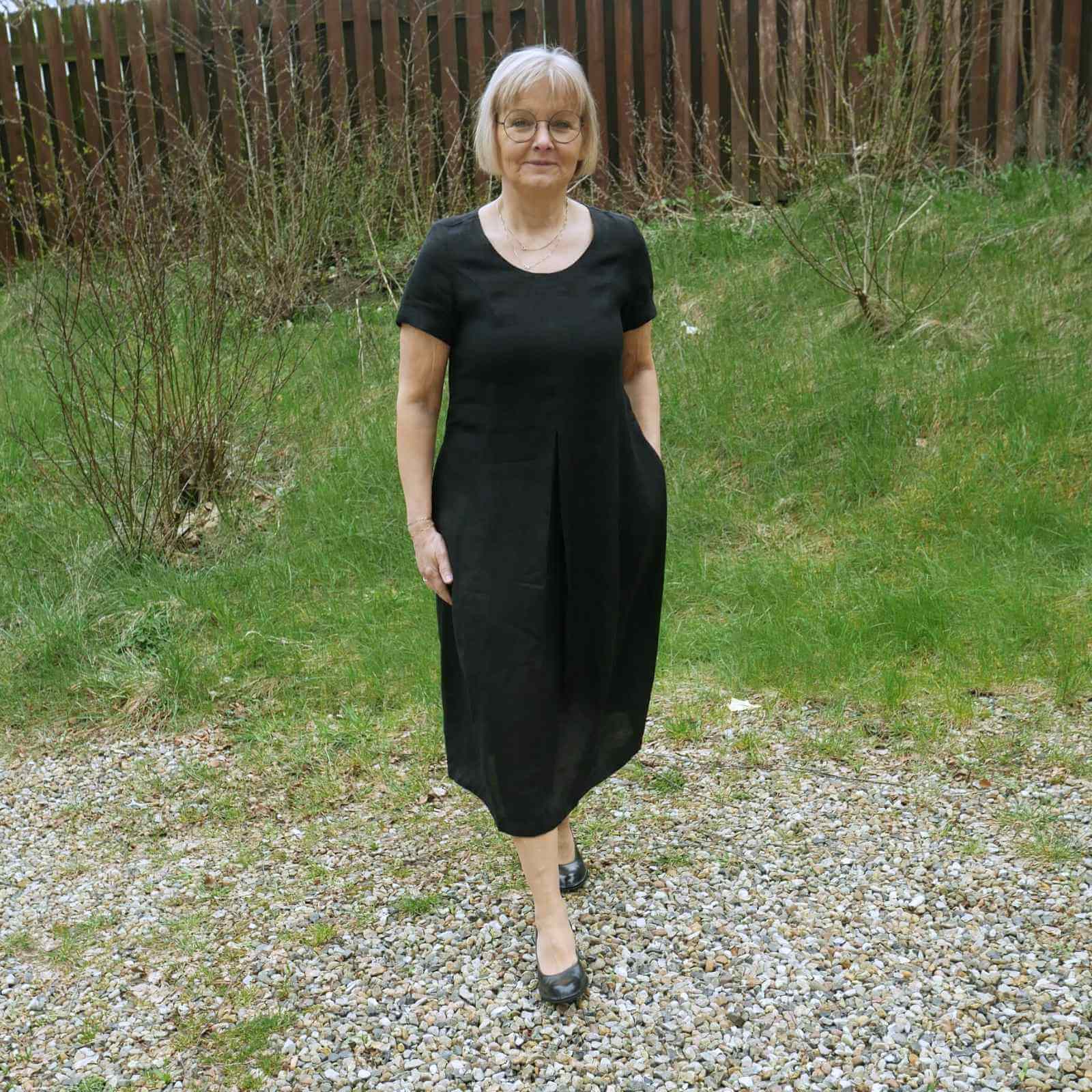 Anbi Jette i sort hørkjole med sorte sko på græs baggrund