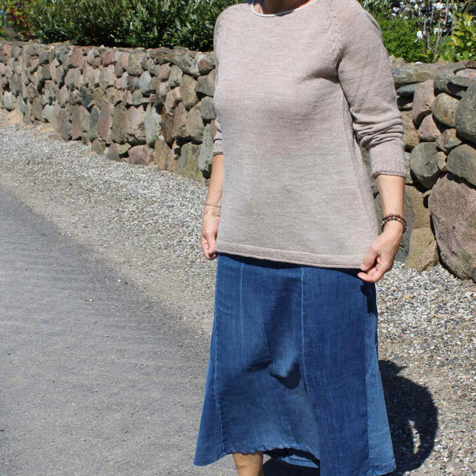 Beige striktrøje med lang jeans nederdel på kvinde foran stenmur