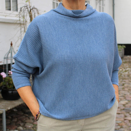 denim lyseblå merinould strikbluse på kvinde foran gods