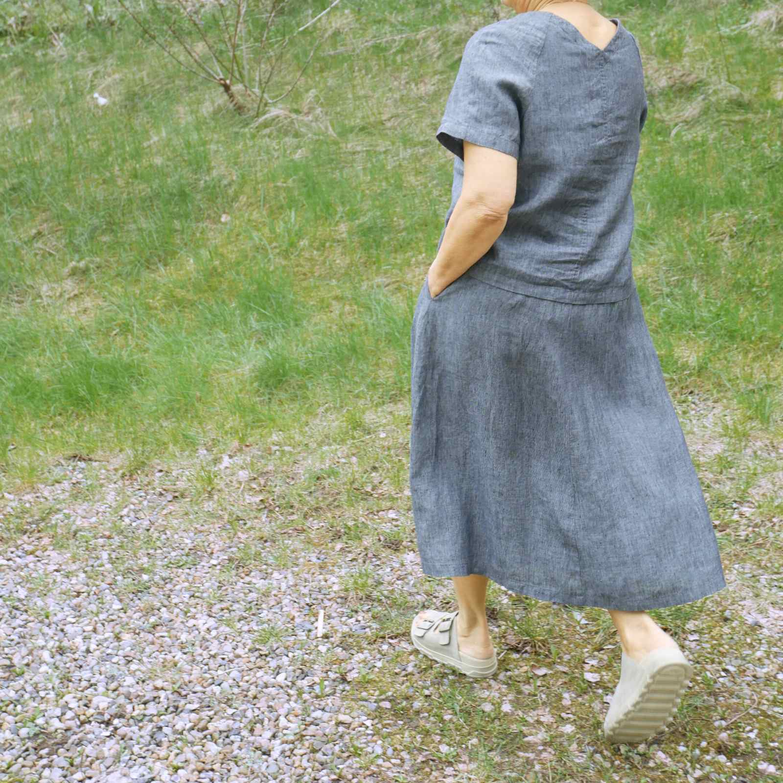Lyseblåt hørsæt bagfra med kortærmet bluse og nederdel på græs baggrund