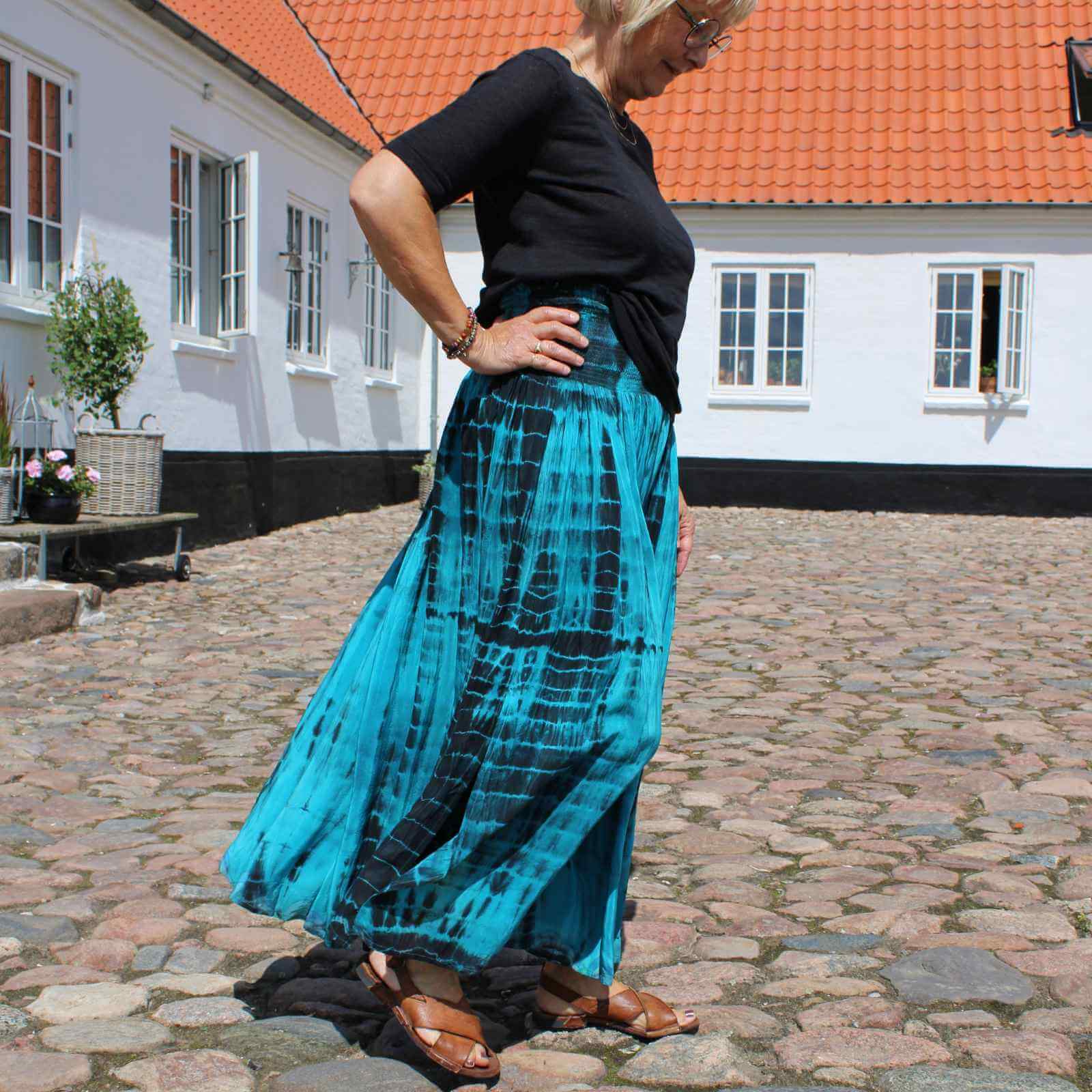 turkis og sort silkenederdel med sort t-shirt på kvinde i gårdhave på gods