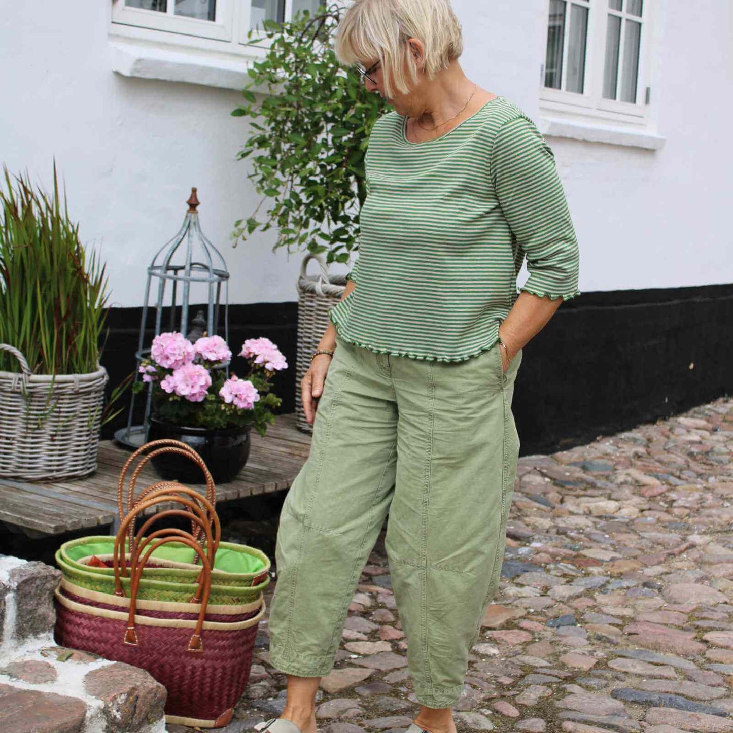 Anbi Jette i lysegrøn stribet økologisk bomuldsbluse og lysegrønne Oska bukser foran Anbi tøjbutik