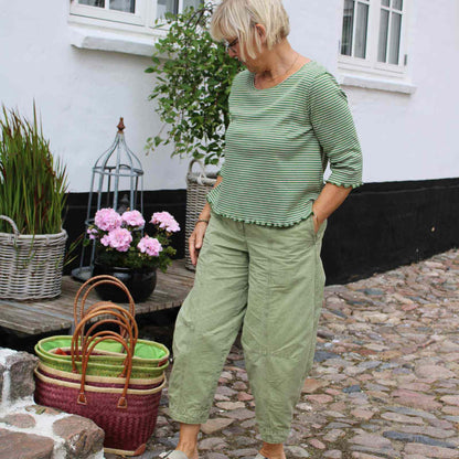 Anbi Jette i lysegrøn stribet økologisk bomuldsbluse og lysegrønne Oska bukser foran Anbi tøjbutik