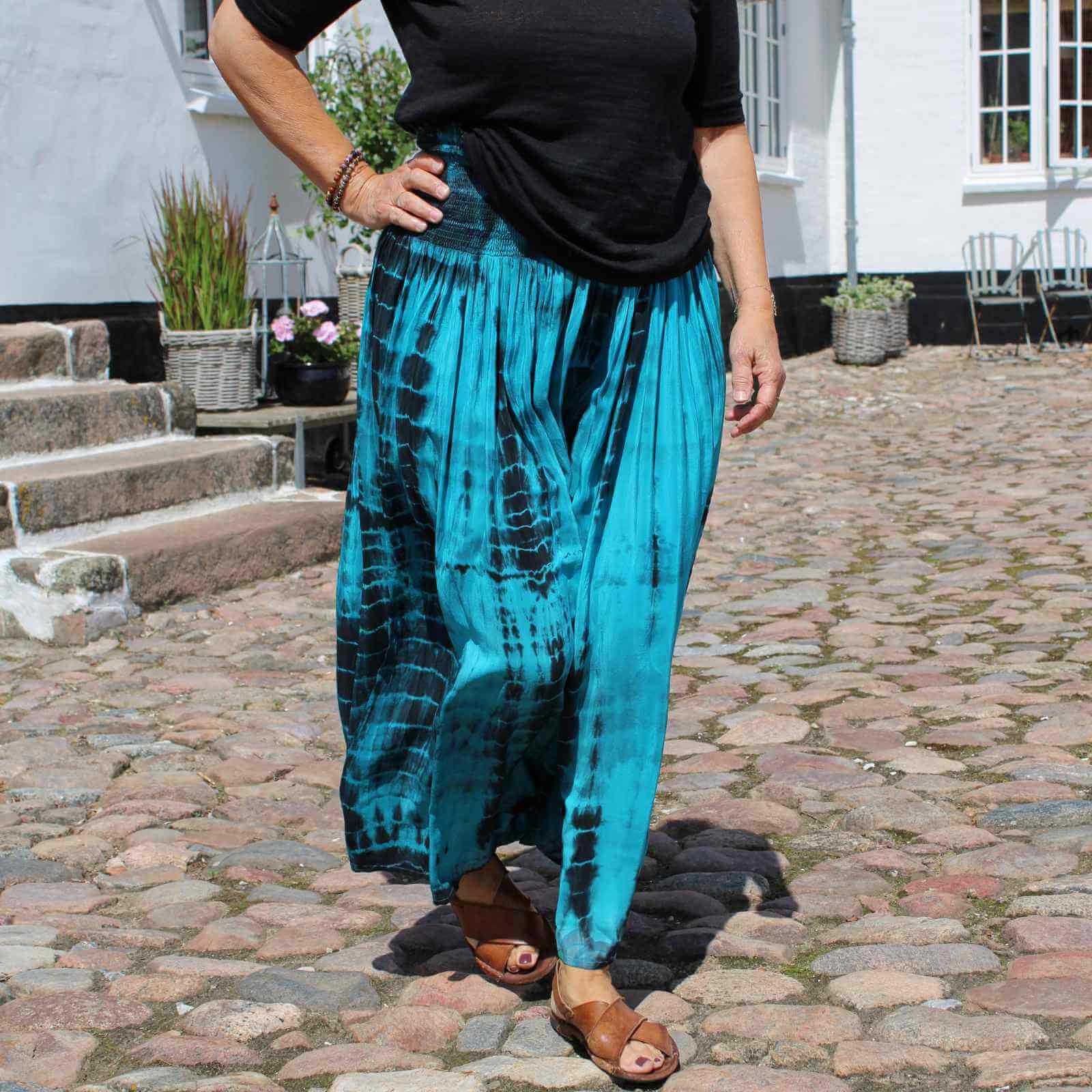 turkis og sort silkenederdel med sort t-shirt, brune sandaler på kvinde i gårdhave på gods