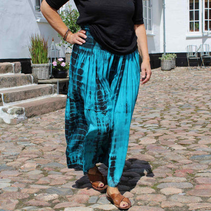 turkis og sort silkenederdel med sort t-shirt, brune sandaler på kvinde i gårdhave på gods